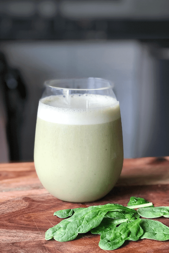 a clear glass on a counter with a light green colored frothy smoothie inside