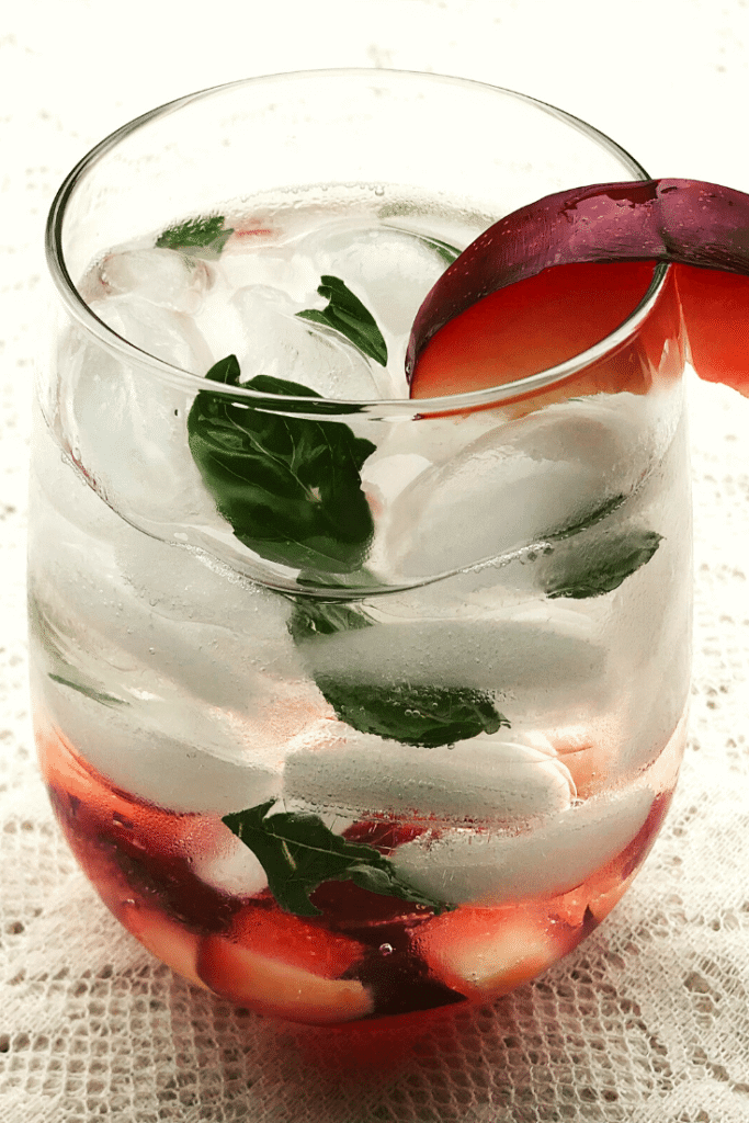 A glass full of ice, plums, basil and clear spirit cocktails 