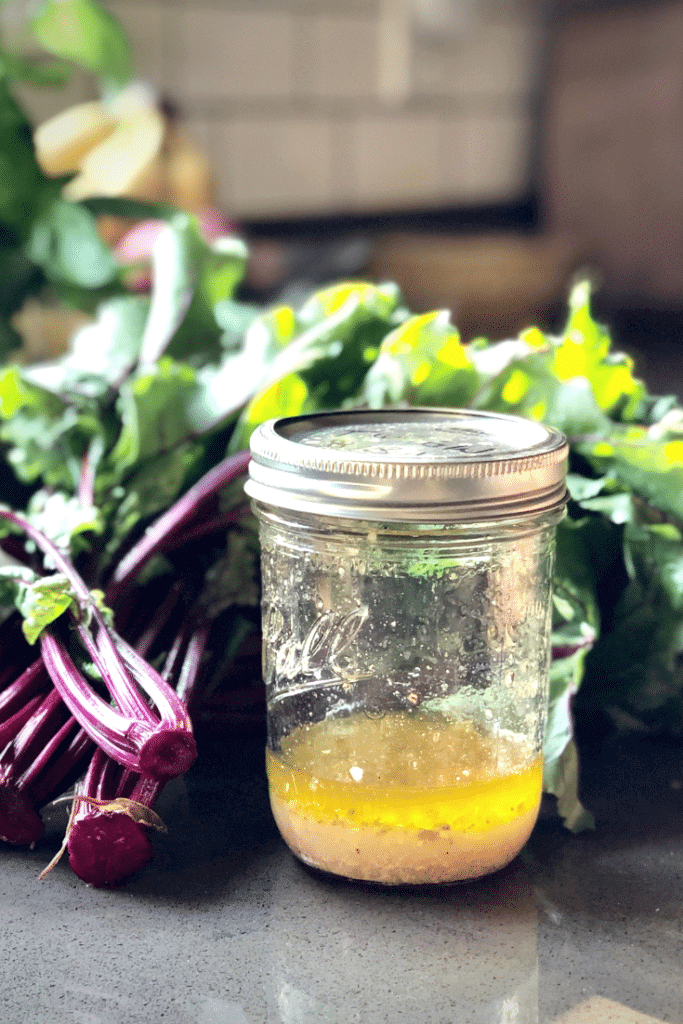 A beautiful mason jar full of bright vinaigrette with beet greens in the background 