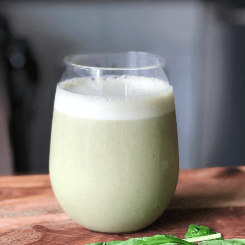a clear glass on a counter with a light green colored frothy smoothie inside