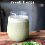 a clear glass on a counter with a light green colored frothy smoothie inside