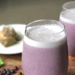 A purple smoothie in a short glass with spinach and blueberries as garnish next to a tea bag