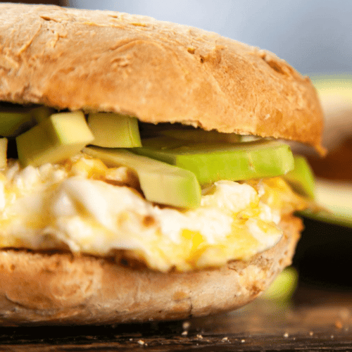 a fluffy egg sandwich on a golden bun with greens and avocado