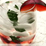 A glass full of ice, plums, basil and clear spirit cocktails